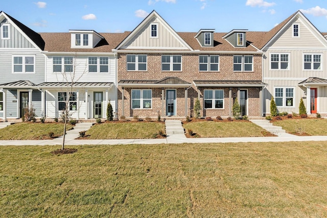 townhome / multi-family property with a front lawn, a standing seam roof, metal roof, brick siding, and board and batten siding