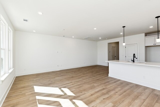 unfurnished living room featuring a sink, light wood-type flooring, baseboards, visible vents, and recessed lighting