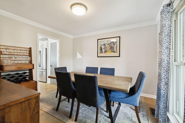 dining space with light wood-type flooring, baseboards, visible vents, and ornamental molding