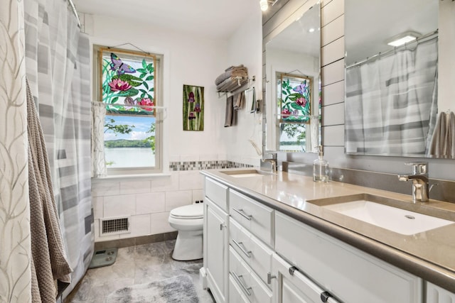 bathroom featuring double vanity, visible vents, toilet, and a sink