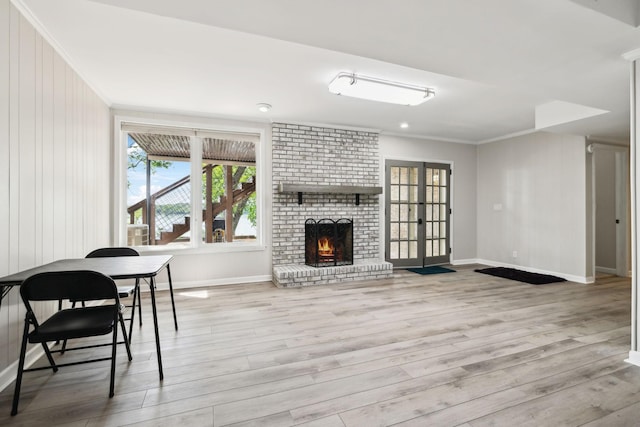 living room featuring light wood finished floors, a brick fireplace, baseboards, and ornamental molding