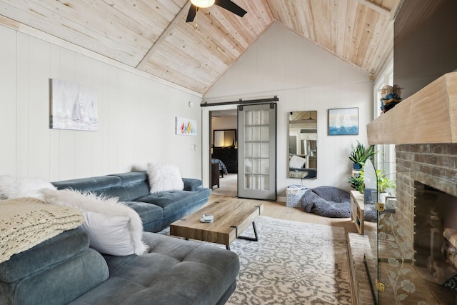 living room with a barn door, a brick fireplace, wood finished floors, ceiling fan, and wood ceiling