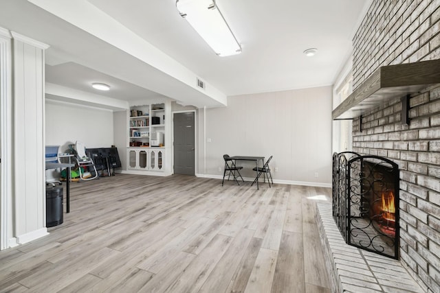 interior space featuring light wood finished floors, visible vents, baseboards, a brick fireplace, and built in features