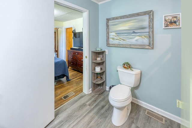 half bathroom with baseboards, wood finished floors, visible vents, and toilet