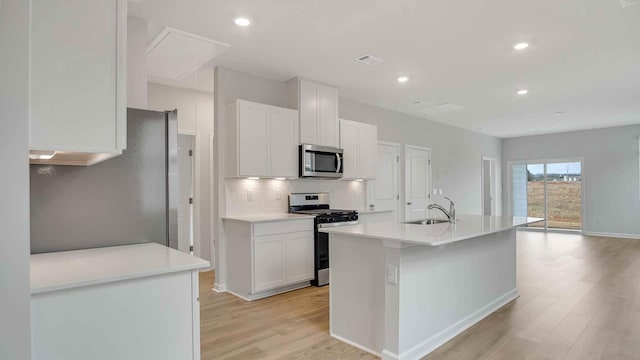 kitchen featuring a sink, tasteful backsplash, white cabinetry, light wood-style floors, and appliances with stainless steel finishes