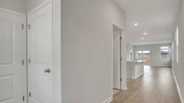 hallway with baseboards, light wood-type flooring, and recessed lighting