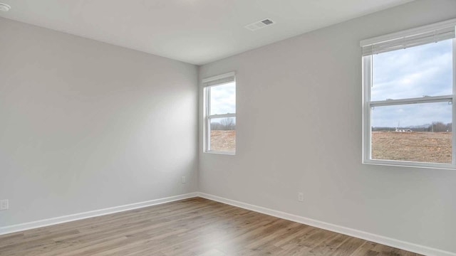 spare room with baseboards, wood finished floors, visible vents, and a wealth of natural light