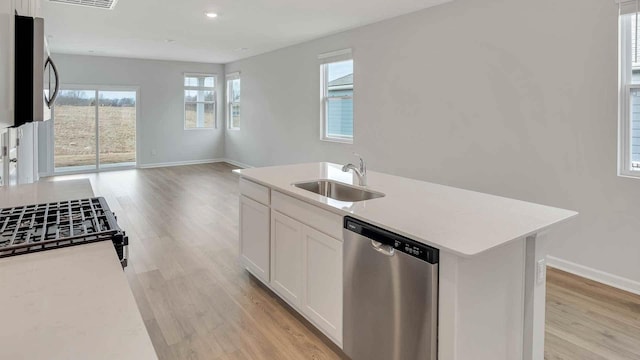 kitchen featuring light wood-style flooring, a sink, open floor plan, light countertops, and appliances with stainless steel finishes