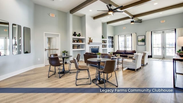 living room featuring beamed ceiling, a stone fireplace, a ceiling fan, and wood finished floors
