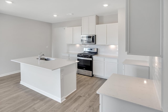 kitchen with a sink, decorative backsplash, a kitchen island with sink, light wood-style flooring, and appliances with stainless steel finishes