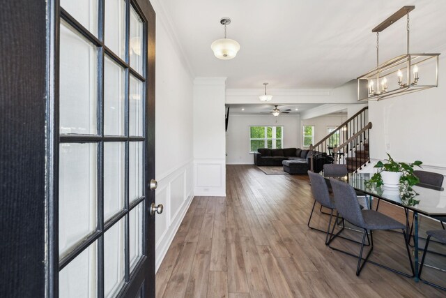 foyer featuring a wainscoted wall, ceiling fan with notable chandelier, wood finished floors, stairs, and crown molding