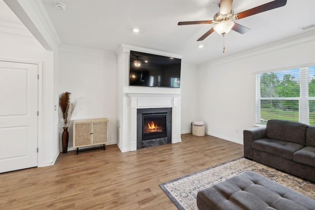 living room with light wood-type flooring, a glass covered fireplace, visible vents, recessed lighting, and ornamental molding