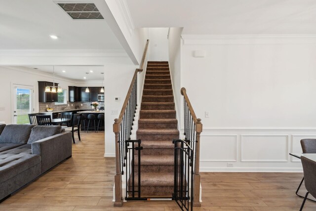 stairs featuring wood finished floors, visible vents, a wainscoted wall, and crown molding