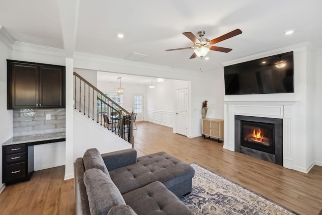 living area featuring a glass covered fireplace, light wood-style floors, a ceiling fan, and stairs