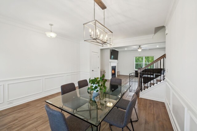 dining area with crown molding, wood finished floors, stairway, a decorative wall, and a lit fireplace