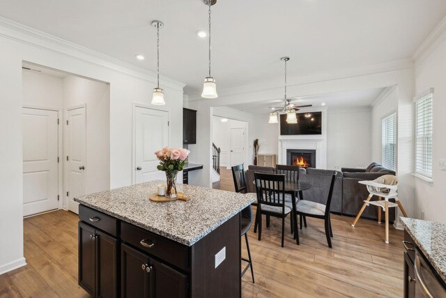 kitchen with light wood-type flooring, crown molding, a lit fireplace, open floor plan, and a breakfast bar area