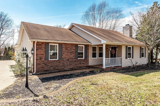 ranch-style home featuring a chimney, a front lawn, a shingled roof, covered porch, and brick siding