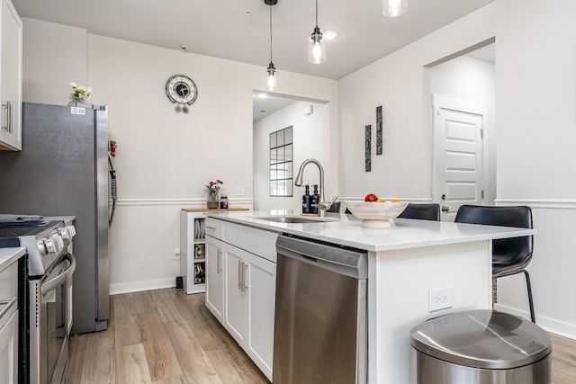 kitchen with a sink, an island with sink, light wood-type flooring, white cabinets, and appliances with stainless steel finishes