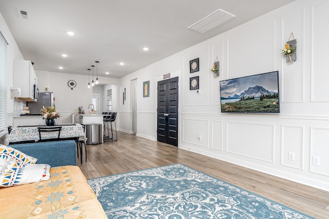 living area with a decorative wall, light wood finished floors, visible vents, and recessed lighting