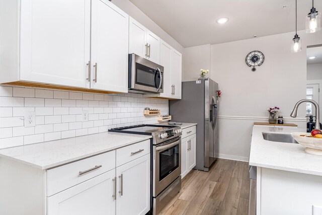 kitchen featuring light wood finished floors, stainless steel appliances, backsplash, a sink, and white cabinetry