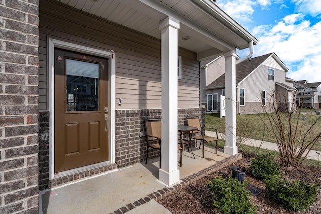 view of exterior entry featuring covered porch and brick siding