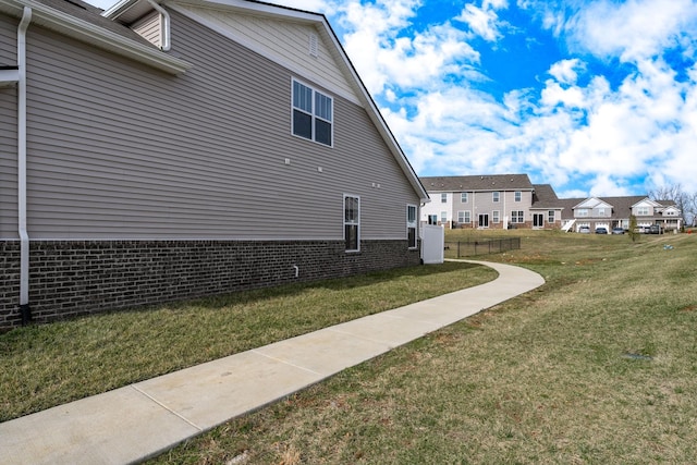 view of home's exterior with fence, a lawn, brick siding, and a residential view