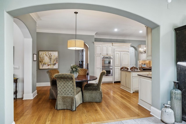 dining space featuring light wood-type flooring, arched walkways, and ornamental molding