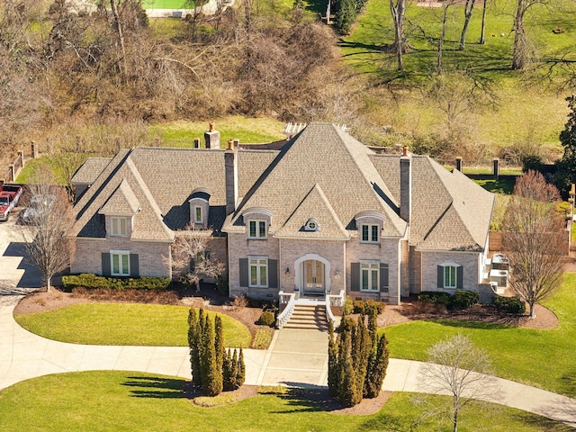 french country inspired facade featuring a front yard, roof with shingles, and a chimney