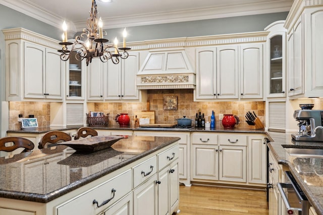 kitchen featuring dark stone countertops, hanging light fixtures, a sink, glass insert cabinets, and premium range hood
