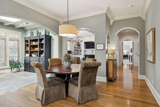 dining room featuring a notable chandelier, arched walkways, ornamental molding, and light wood finished floors