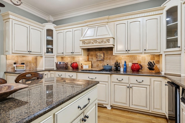 kitchen featuring dark stone counters, custom exhaust hood, stainless steel gas stovetop, glass insert cabinets, and cream cabinetry