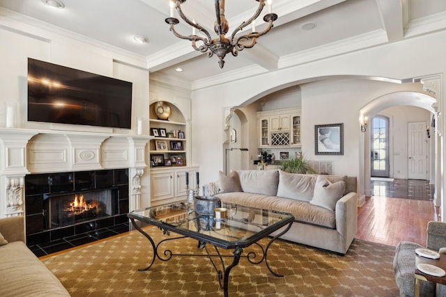 living area featuring crown molding, arched walkways, a tiled fireplace, coffered ceiling, and beam ceiling