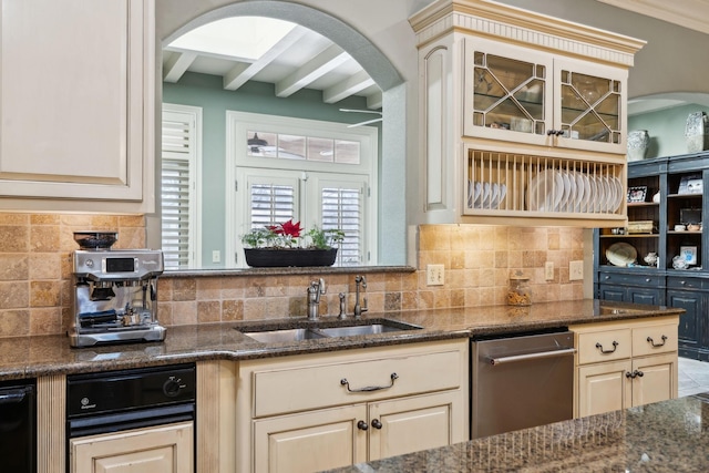 kitchen featuring arched walkways, cream cabinetry, stainless steel dishwasher, and a sink