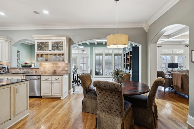 dining room with arched walkways, light wood-style flooring, and ornamental molding