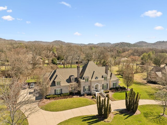 view of front facade featuring a mountain view, stone siding, a chimney, concrete driveway, and a front yard