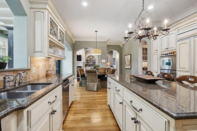kitchen with light wood finished floors, ornamental molding, a sink, a center island, and appliances with stainless steel finishes