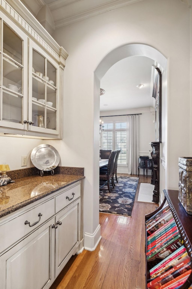 bar featuring arched walkways, light wood-style flooring, and crown molding
