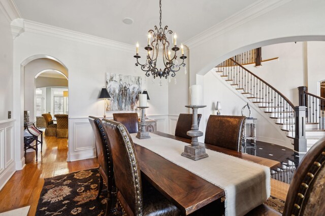 dining space featuring arched walkways, a chandelier, wood finished floors, stairs, and ornamental molding
