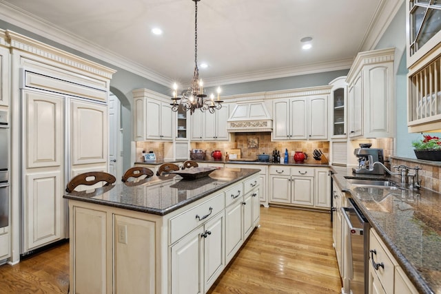 kitchen with custom exhaust hood, a sink, an inviting chandelier, light wood-style flooring, and appliances with stainless steel finishes