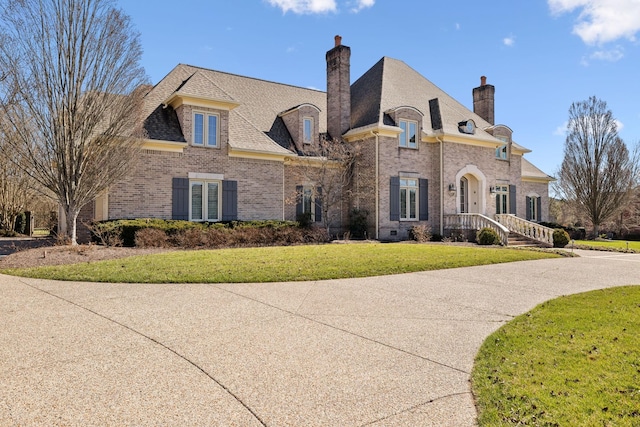 french country style house featuring a front lawn, brick siding, and a chimney