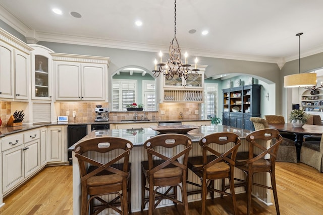 kitchen with arched walkways, a kitchen bar, a chandelier, glass insert cabinets, and pendant lighting