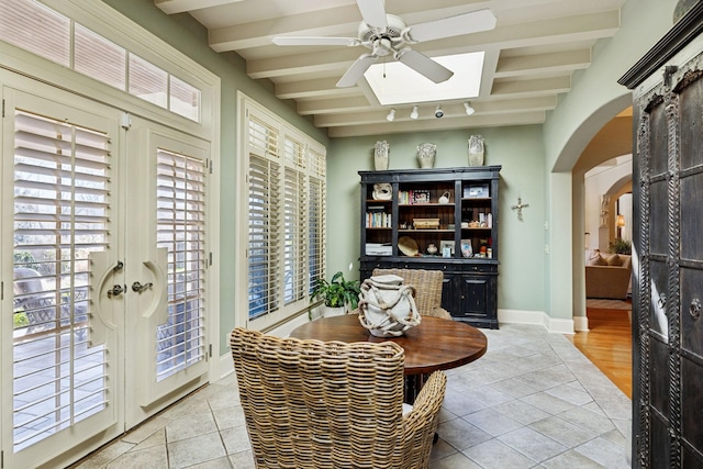 interior space with baseboards, arched walkways, a ceiling fan, and light tile patterned floors