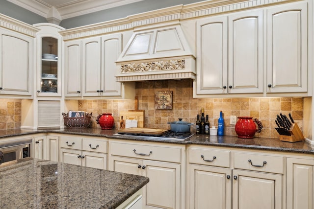 kitchen featuring crown molding, dark stone countertops, glass insert cabinets, custom range hood, and cream cabinetry