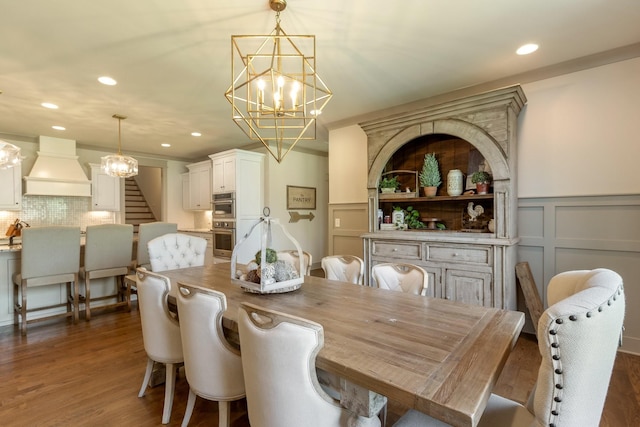 dining space featuring a chandelier, stairway, dark wood-style floors, and a decorative wall