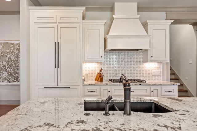 kitchen with light stone countertops, a sink, stainless steel gas stovetop, decorative backsplash, and premium range hood