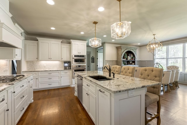 kitchen featuring a wainscoted wall, a sink, a notable chandelier, appliances with stainless steel finishes, and a breakfast bar area