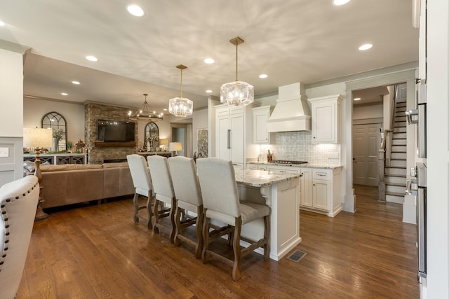 kitchen featuring backsplash, white cabinetry, visible vents, open floor plan, and premium range hood