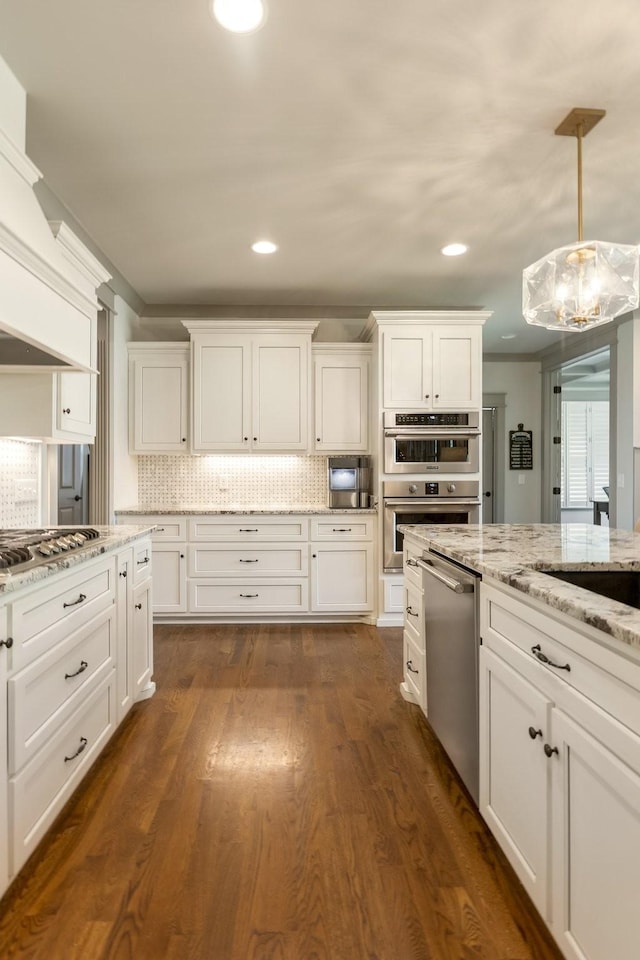 kitchen featuring white cabinets, light stone counters, backsplash, premium range hood, and appliances with stainless steel finishes