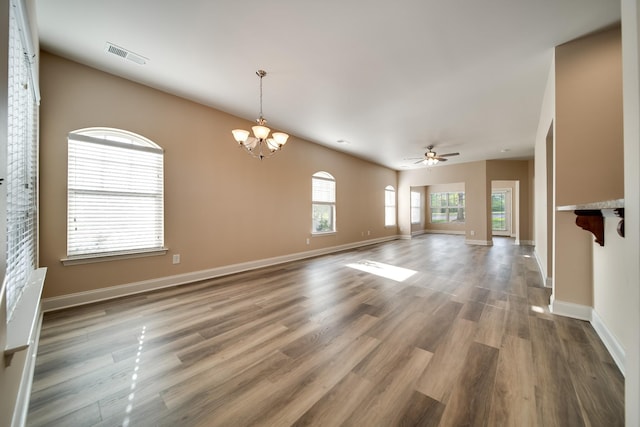 unfurnished living room with ceiling fan with notable chandelier, baseboards, wood finished floors, and visible vents