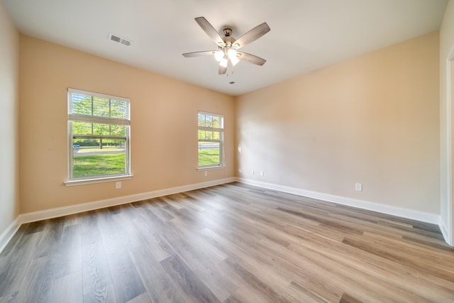 spare room with wood finished floors, visible vents, a ceiling fan, and baseboards